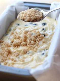 a spoon with some food in it on top of a pan filled with batter and blueberries