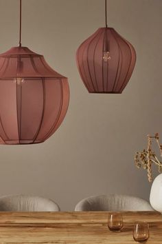 three pink lamps hanging over a wooden table