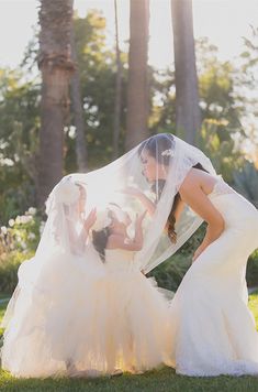 two women in wedding gowns standing next to each other with veil over their heads