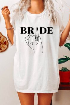 a woman wearing a white t - shirt with the word bride written on it and a finger pointing up