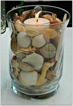 a candle that is inside of a glass vase filled with seashells and sea shells