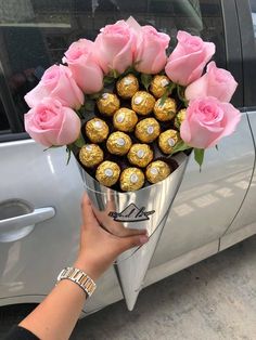 a bouquet of pink roses and chocolates in a silver vase next to a car