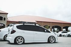 a small white car parked in front of a building with skis on the roof