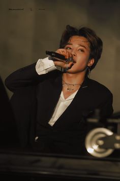 a person that is holding a microphone in their hand and wearing a black suit with white shirt