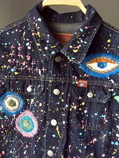 a denim jacket with an eye on it and splattered paint all over the front