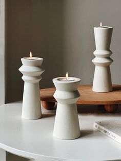 three white candles sitting on top of a table next to a book and candle holder