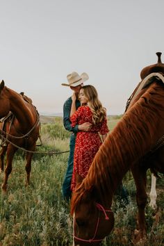 a man and woman standing next to two horses in a field with one holding the other's head