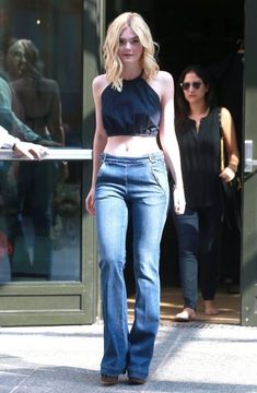 a woman in high waisted jeans is walking down the street with her hand on her hip