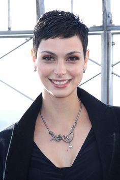 a woman with short hair wearing a black jacket and smiling at the camera while standing in front of a metal structure