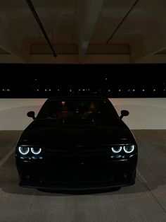 a black sports car is parked in a parking garage with its headlights turned on at night