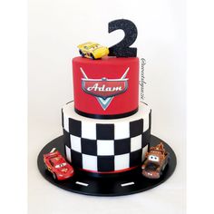 a two tier cake with cars on it and the number 2 on top is decorated in black, white, and red