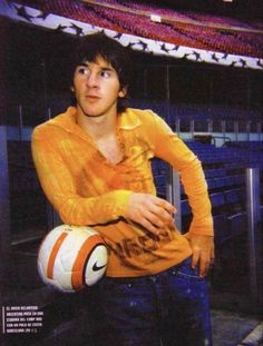 a man in an orange shirt holding a white and orange soccer ball at a stadium