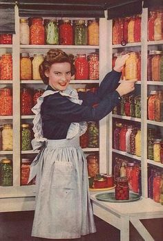 a woman standing in front of a shelf filled with jars