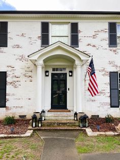 an american flag hangs on the front door of a white brick house