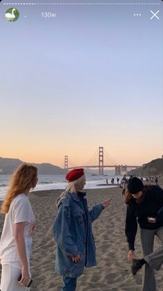 three people are standing on the beach and one is flying a kite