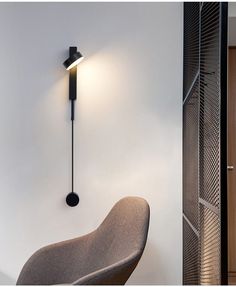 a modern wall light mounted on the side of a white wall next to a chair