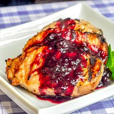 grilled chicken with blueberry sauce on a white square plate, garnished with green leaves