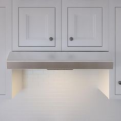 a kitchen with white cabinets and an oven hood over the stove top in front of it