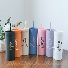 six different colored tumblers with straws in them on a table next to a potted plant