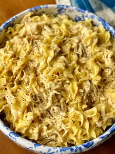 a blue and white bowl filled with pasta on top of a wooden table next to a napkin