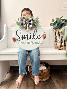 a young boy sitting on a bench holding a sign that says smile jesus loves you