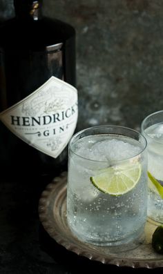 two glasses filled with ice and limes next to a bottle of hendrick gin