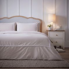 a bed with white linens and pillows in a small room next to a night stand