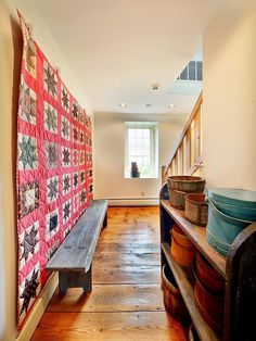 a wooden bench sitting in the middle of a room next to a wall with a quilt on it