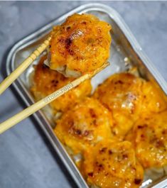 some food in a metal container with chopsticks