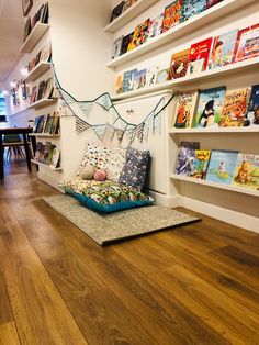 a room filled with lots of books on shelves next to a floor covered in pillows