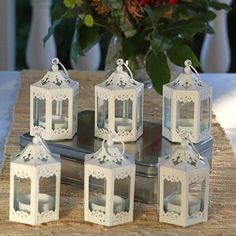 four white lanterns sitting on top of a table next to a vase with red flowers