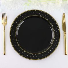 a black plate with gold dots on it next to a fork and knife, along with a white lace table cloth