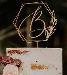 a white cake topped with a gold monogrammed letter b and a single rose