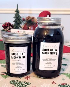 two jars of root beer moonhine sitting on a table next to a christmas tree