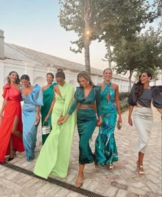 several women are walking down the sidewalk in different colored dresses and one is carrying a purse