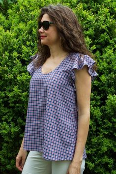 a woman standing in front of some bushes wearing sunglasses and a plaid top with ruffle sleeves