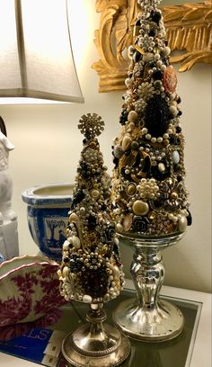 two small christmas trees sitting on top of a table next to a vase and lamp