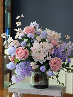 a vase filled with pink and purple flowers on top of a wooden table next to a mirror