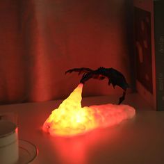 a glowing dragon figurine sitting on top of a table next to a cup