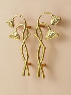 two gold toned metal flower and leaf shaped hooks on a beige wall with a light pink background