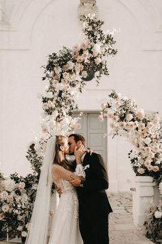 a bride and groom kissing in front of a floral arch