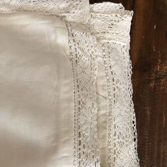 white linen with crochet lace on it sitting on a wooden table next to a piece of wood