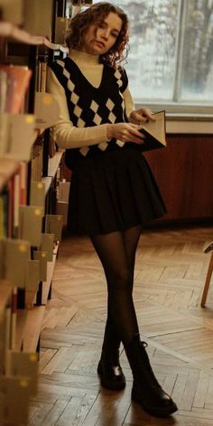 a woman in a black and white sweater is standing near bookshelves holding a book