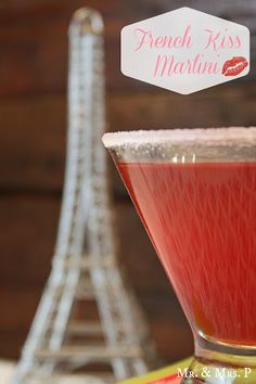 a red drink in a glass next to the eiffel tower with a sticker that says french kiss martini