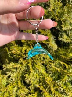 a hand holding a blue glass bird keychain in front of some green plants