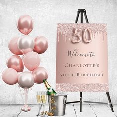 a pink 50th birthday sign with champagne and balloons