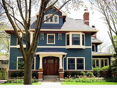 a blue house with white trim and brown door is shown in the foreground, surrounded by trees