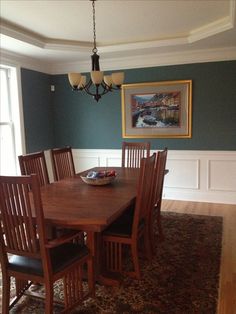 a dinning room table and chairs in front of a window with a painting on the wall