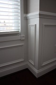 the corner of a room with white painted walls and wood flooring, along with a window