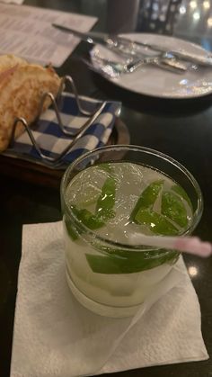 a drink with limes and ice sits on a napkin next to a slice of bread